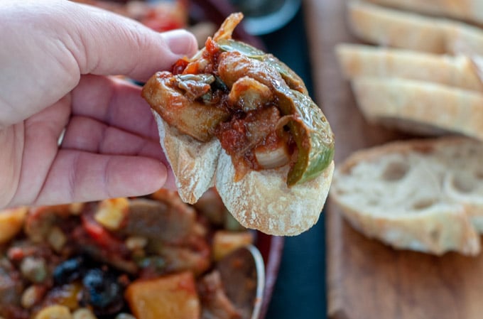 hand holding caponata on a piece of bread