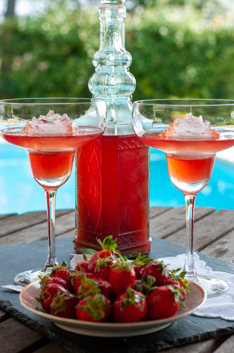 homemade strawberry liqueur in a bottle and 2 glasses served with fresh strawberries