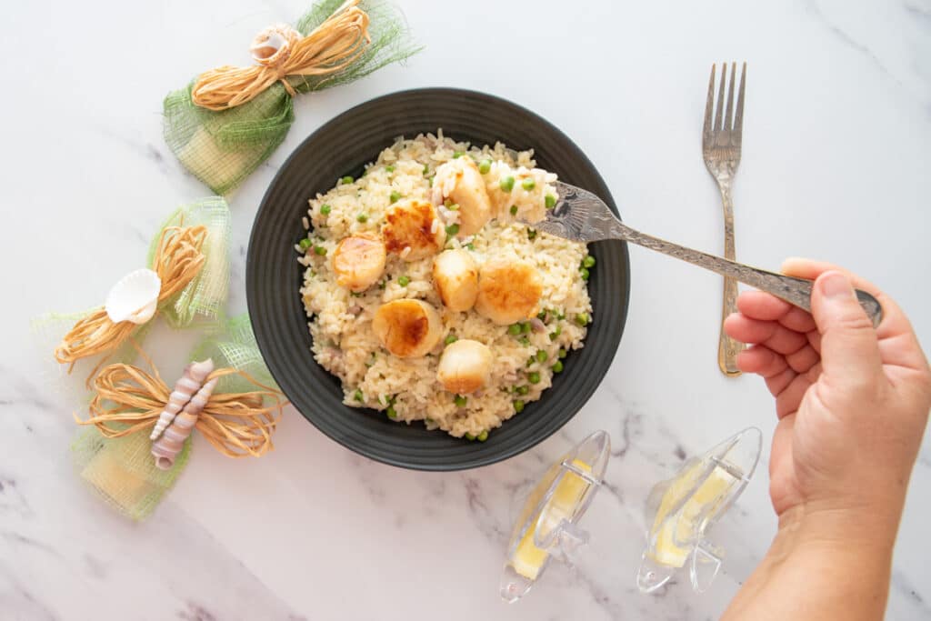 Pan-seared scallops served on top of a risotto with bacon and peas. A fork serving a bite