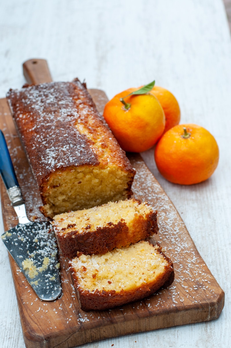 Orange cake loaf on a cutting board with two slices. Oranges on the side
