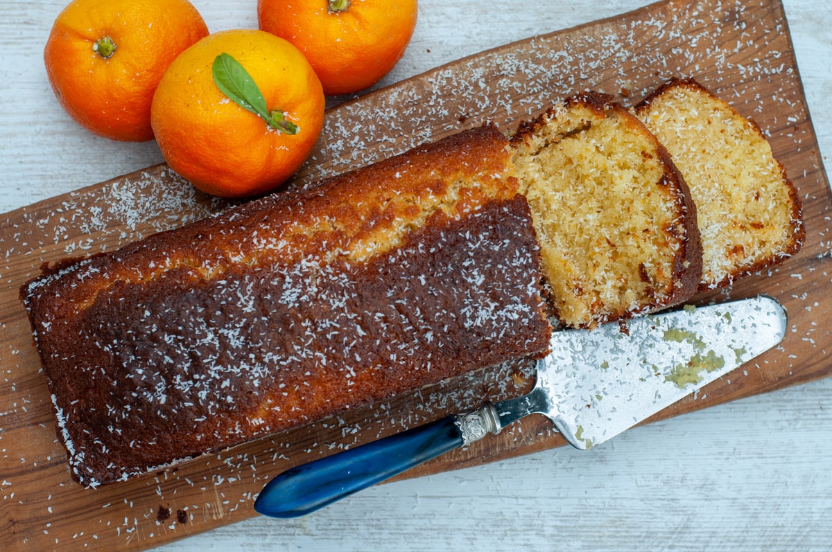 Orange cake over a cutting board two slices cut and sprinkled with coconut
