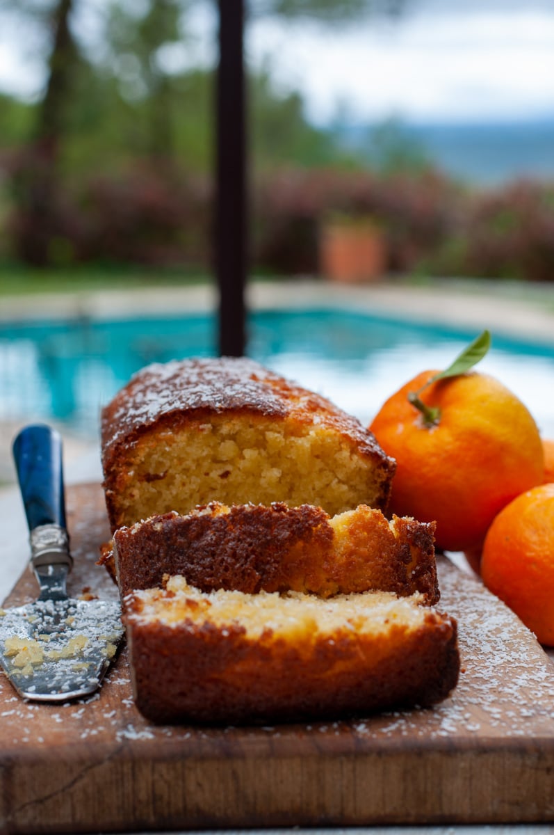 Orange loaf cake on a cutting board two slices cut and the pool in the background