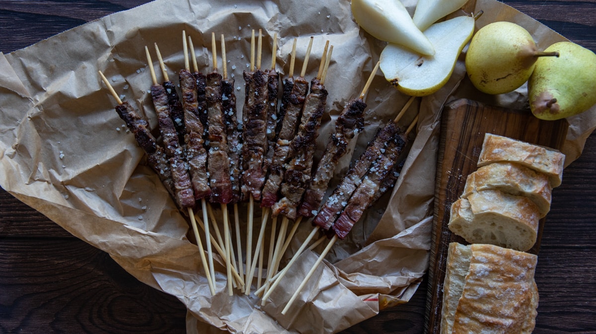 mutton arrosticini on a paper with pear and stale bread