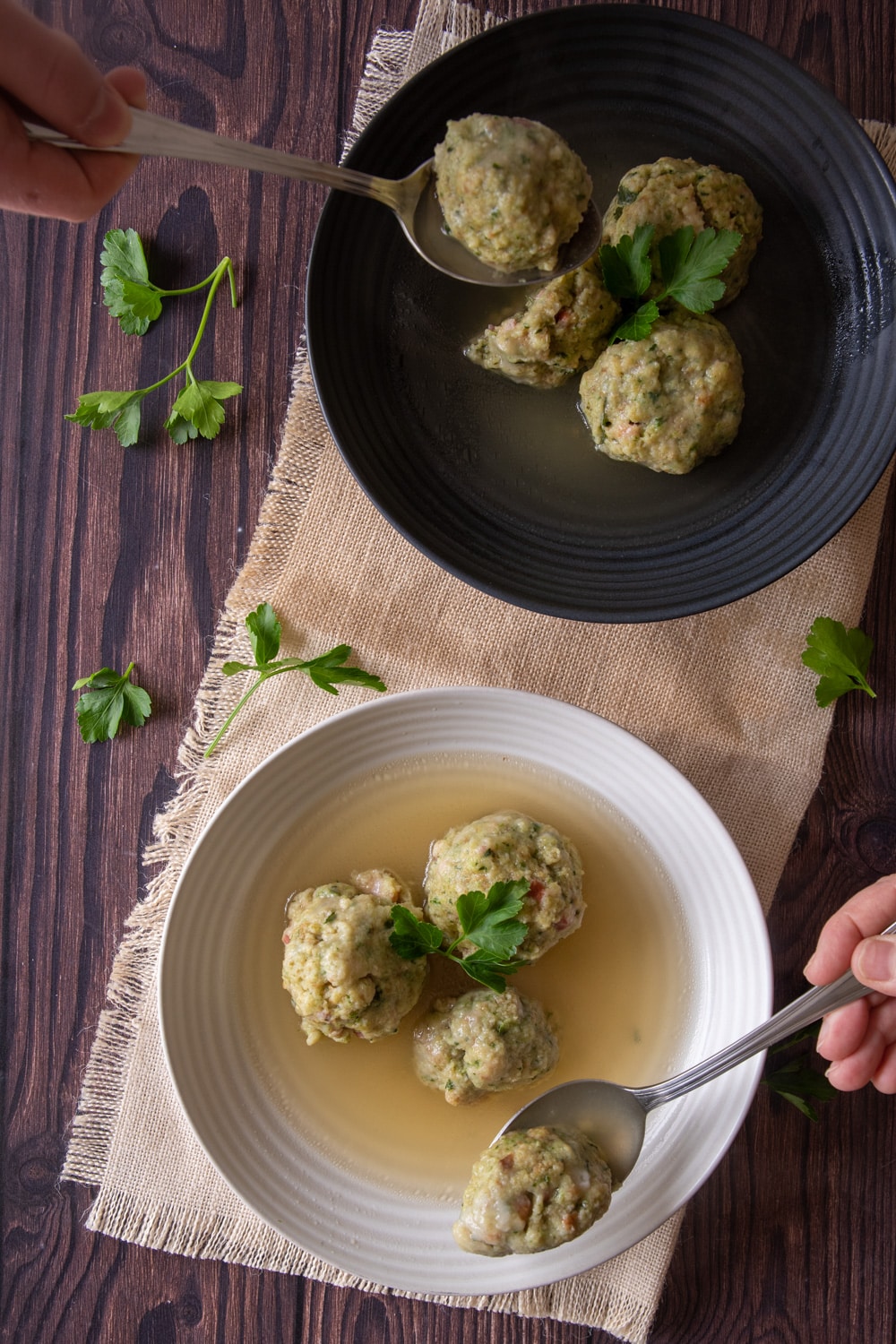Canederli Italian Bread Dumplings served with broth in back and white plates, a spoon cutting them in half