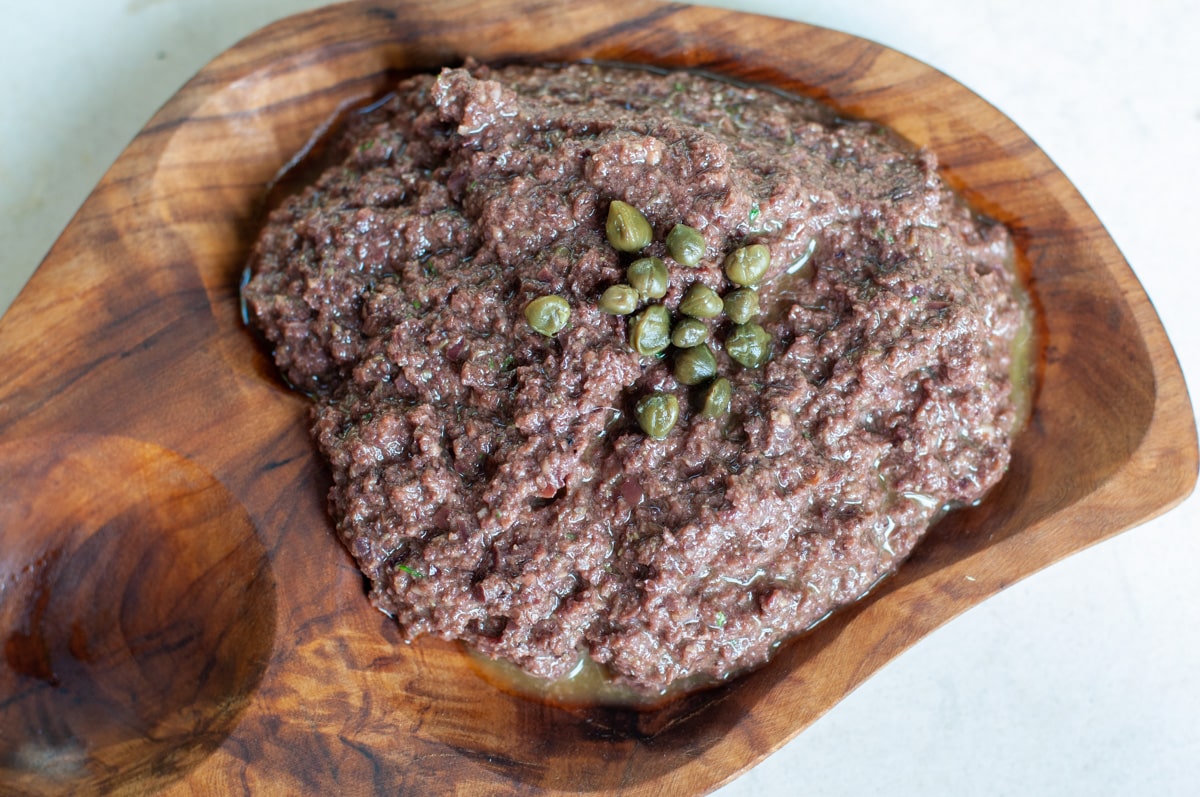 Black olive Tapenade served on a wooden bowl topped with capers