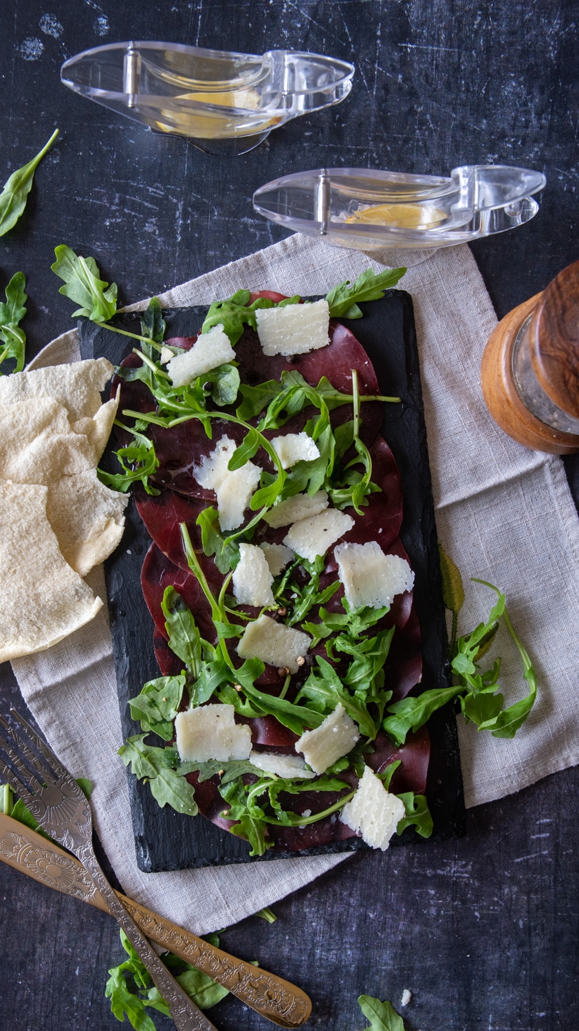 Italian Beef Bresaola on a cutting board served with arugula and parmesan cheese