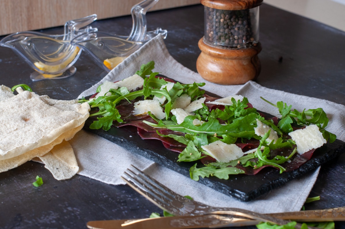 Italian Beef Bresaola on a cutting board served with arugula and parmesan cheese
