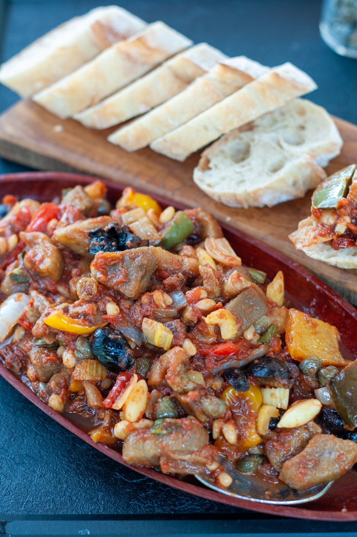 Vegetable caponata served on a try with some crusty bread in the background