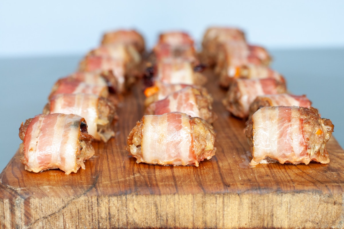 sausage stuffing wrapped in bacon over on a cutting board