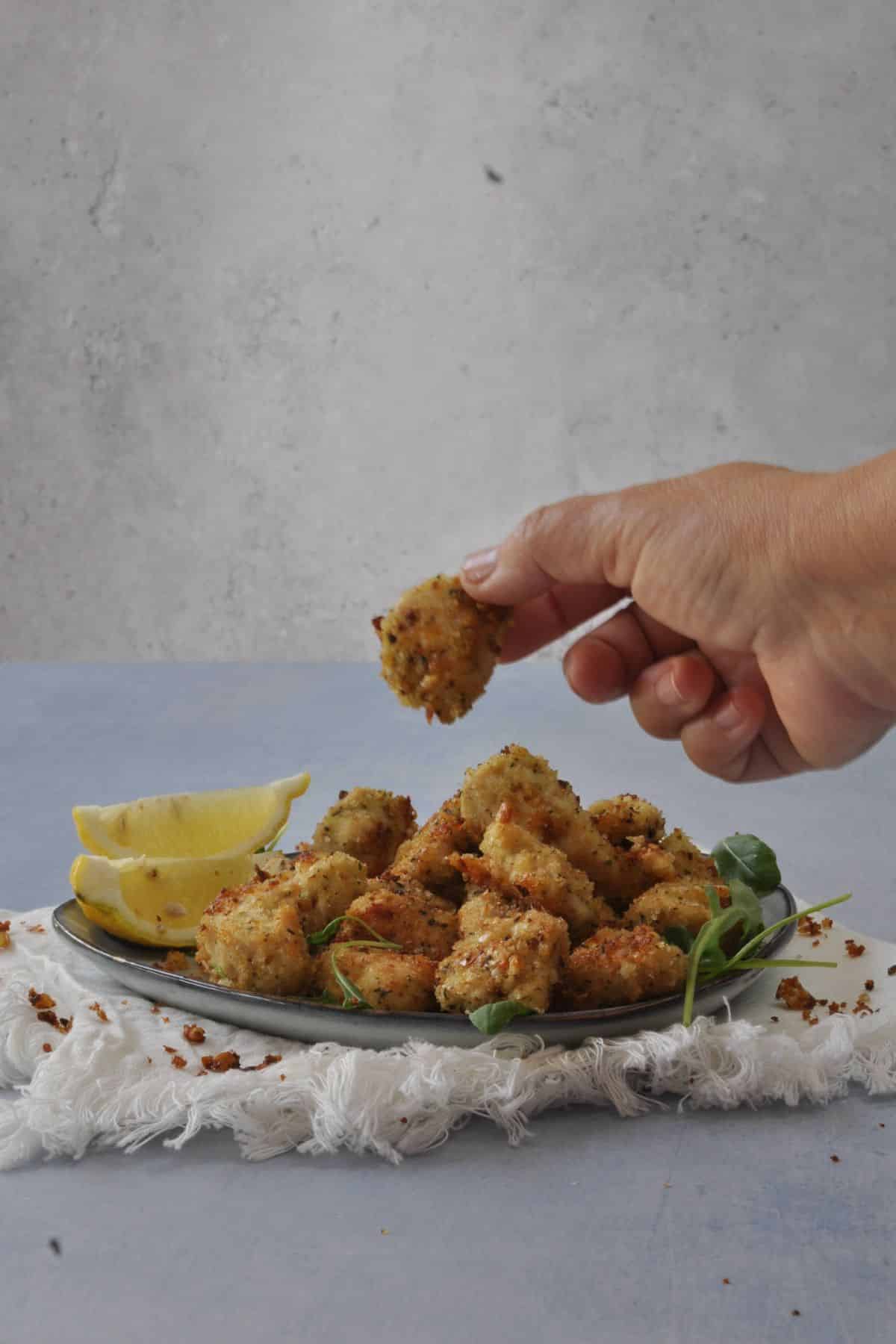 A hand picking up a baked chicken nugget